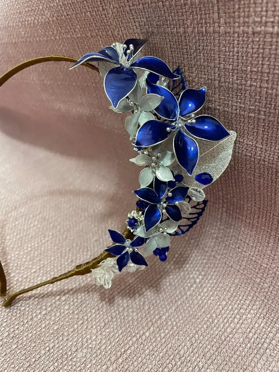 Diadema floral azul y plateada sobre superficie rosa.
