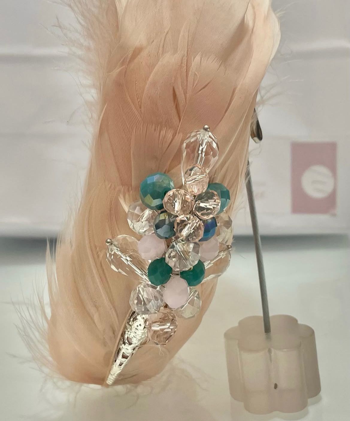 Pluma rosa con adornos de plata y joyas, sobre un expositor transparente.