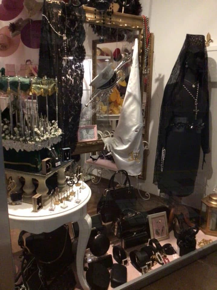 Un escaparate con ropa negra, joyas y sombreros en maniquíes y estantes.