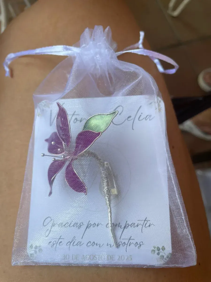A white gift bag holding a silver flower pin on a card that says