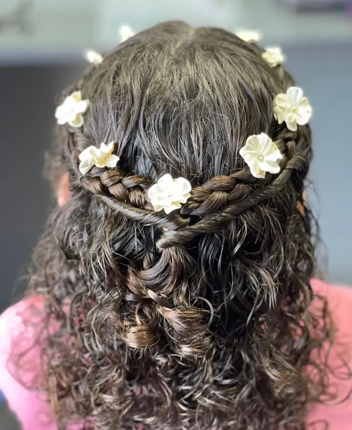 Peinado trenzado con detalles de flores blancas. Cabello oscuro y rizado.