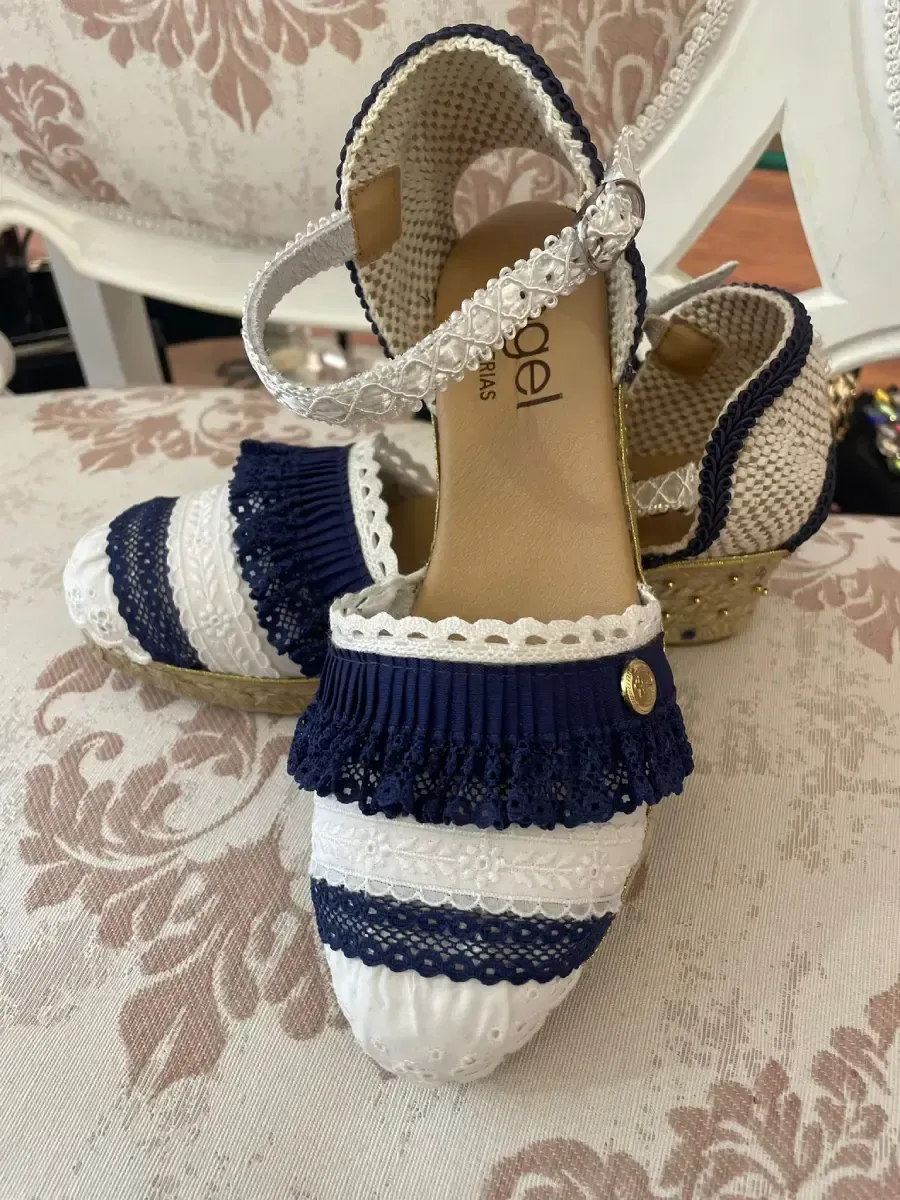 Sandalias de alpargatas de rayas azules y blancas con ribete azul marino y tiras adornadas sobre una superficie estampada.