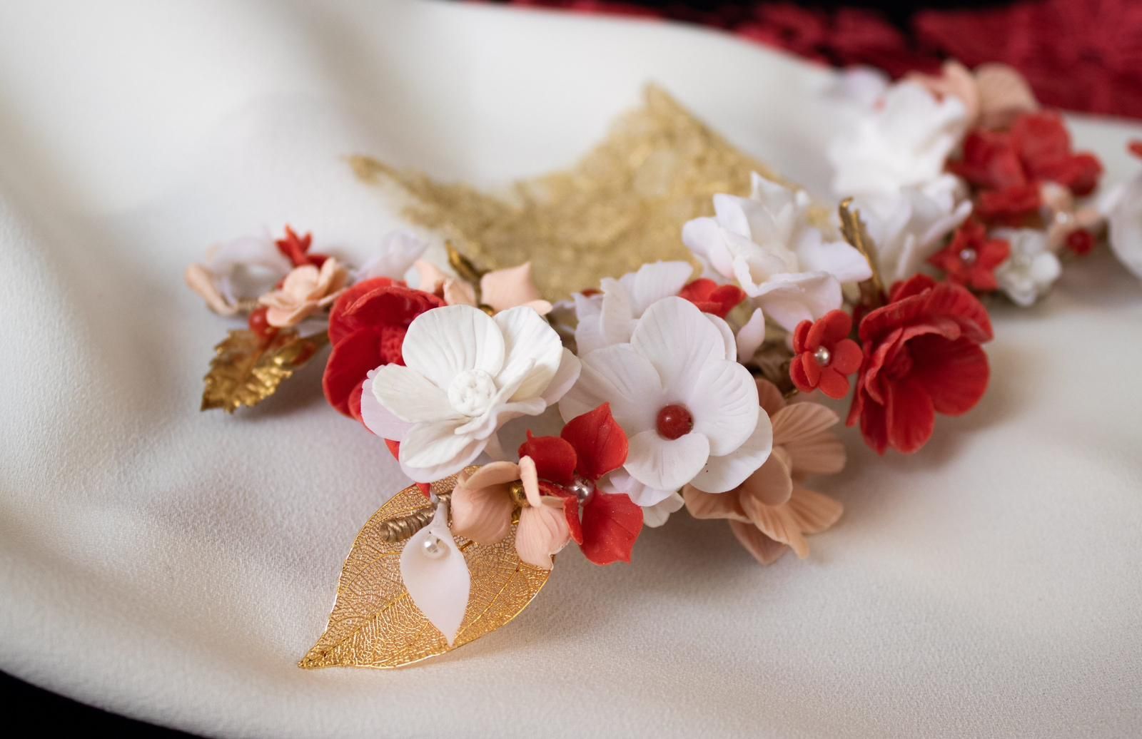 Postizo floral con flores rojas, blancas y doradas sobre una superficie blanca.