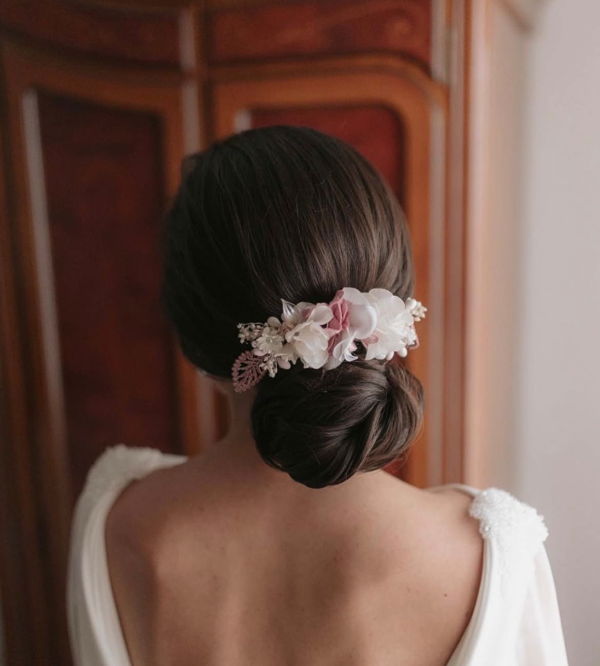 Mujer de cabello oscuro recogido en un moño bajo, adornada con un tocado floral, con un vestido blanco.