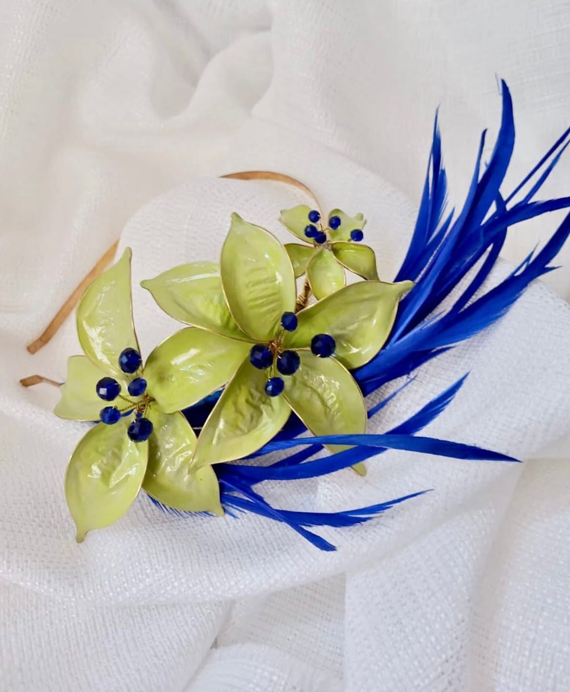 Accesorio para el cabello con flores verdes, plumas azules y cuentas azul oscuro.