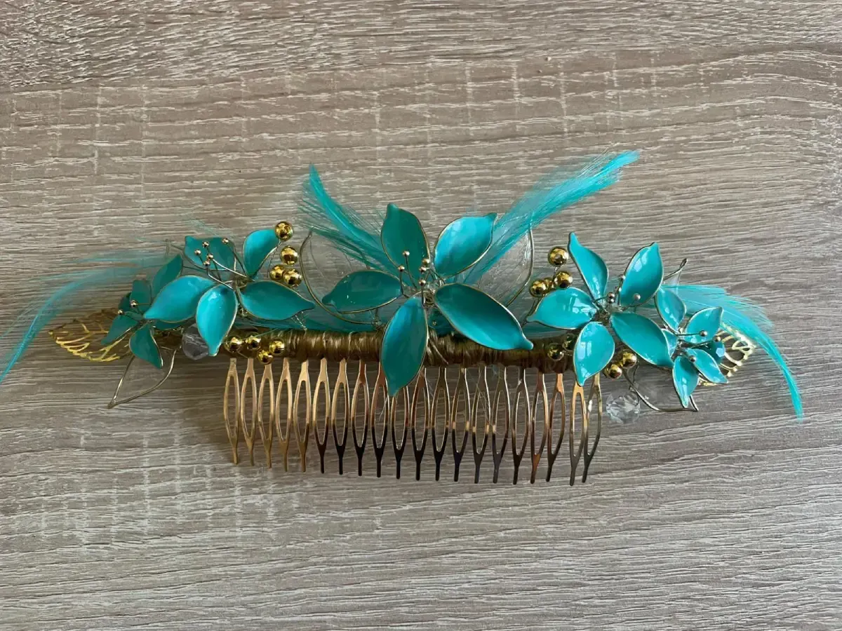 Peineta floral color verde azulado con detalles dorados y plumas.