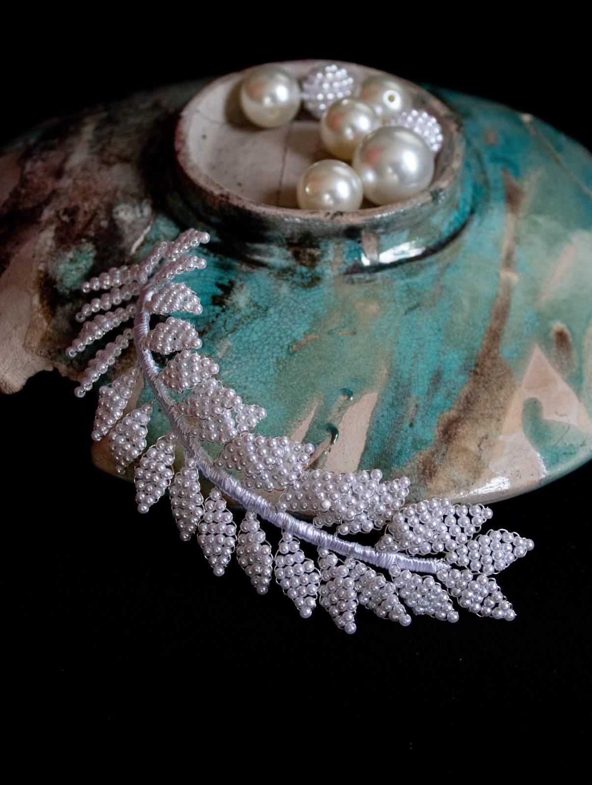 Hoja de cuentas de plata con perlas en un recipiente turquesa sobre fondo negro.