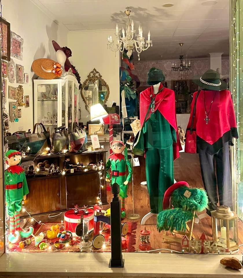 Un escaparate de tienda vintage con adornos navideños y atuendos de elfos.