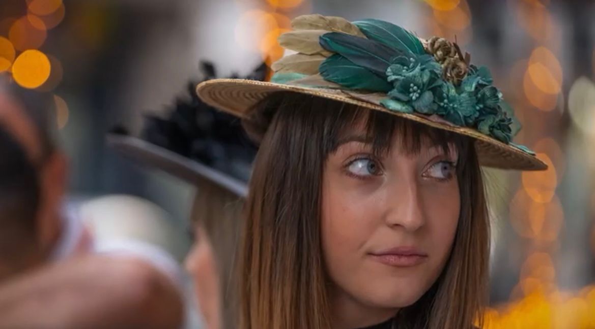 Mujer con sombrero de paja decorado con plumas verdes, mirando fuera de cámara.