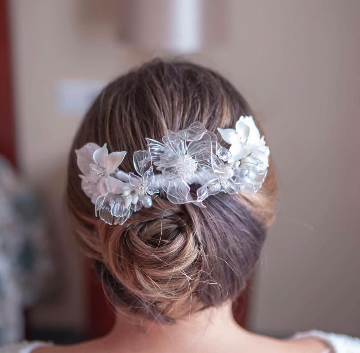 Mujer con cabello castaño peinado en un moño bajo, adornado con un peine floral transparente.