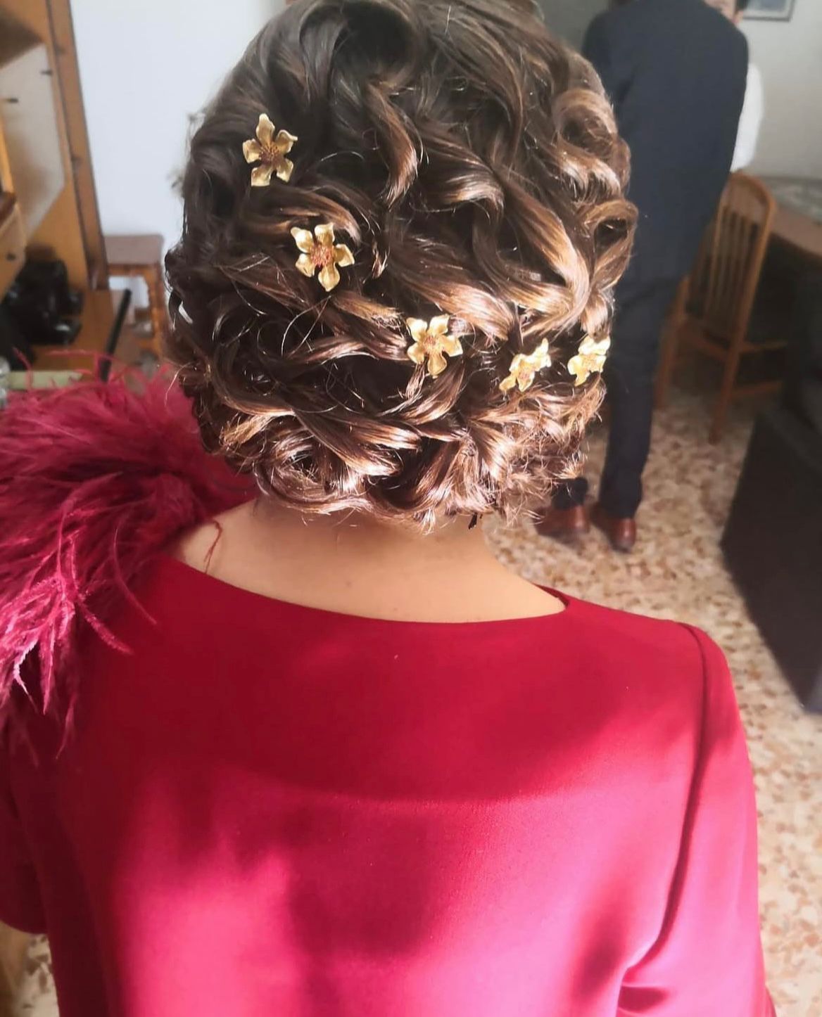 Mujer con vestido rojo, con peinado recogido rizado adornado con broches de flores doradas.