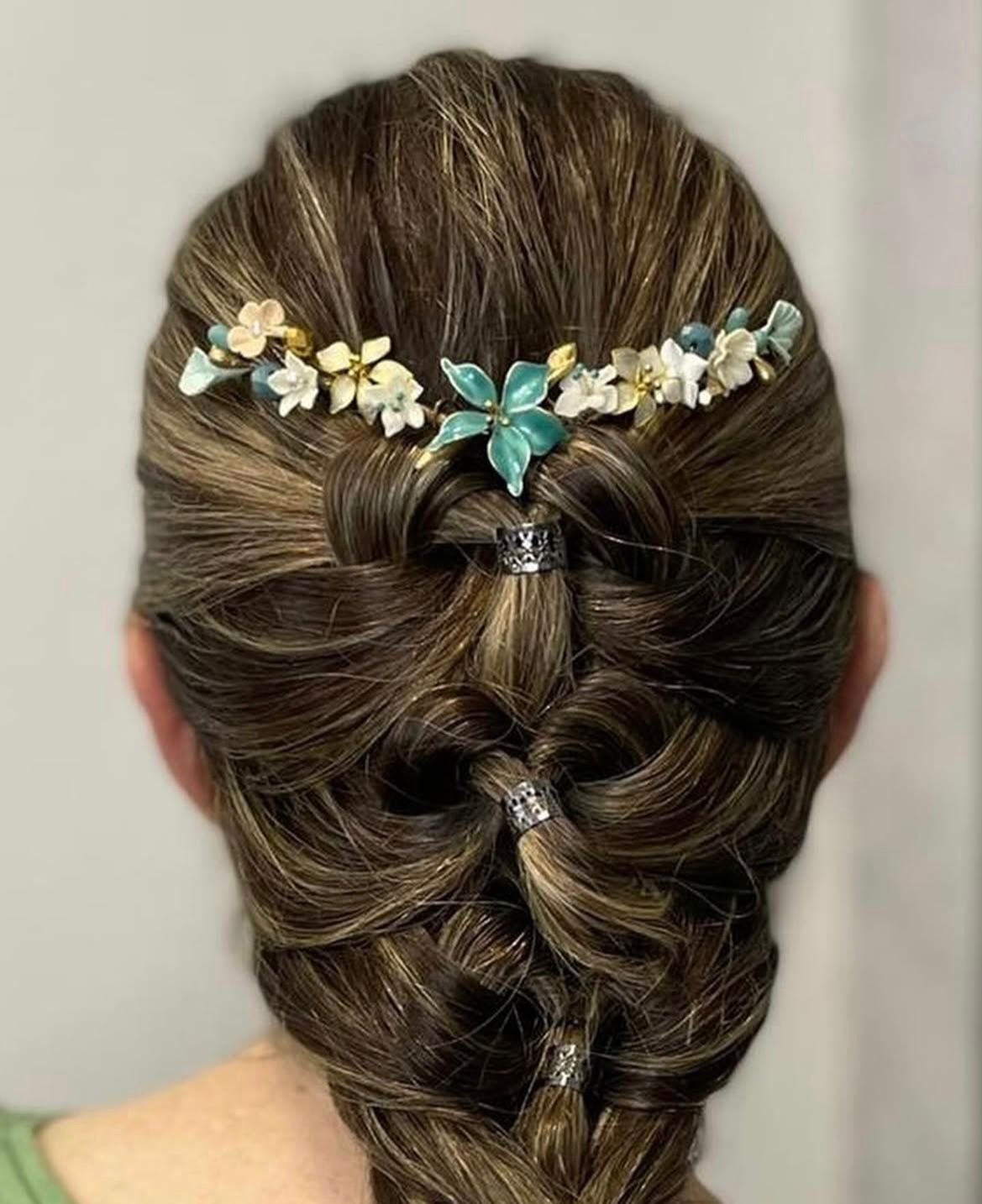 Cabello de mujer peinado en trenza, adornado con un tocado floral; la trenza presenta detalles plateados.