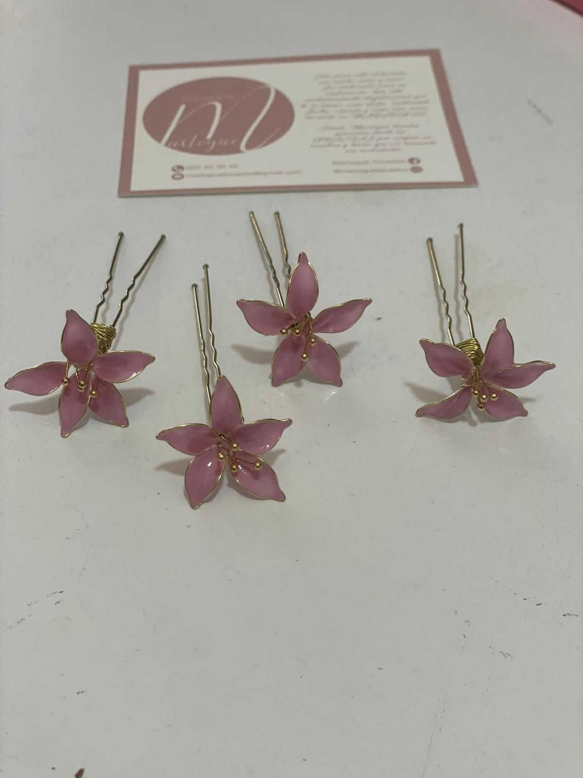 Cuatro horquillas con flores rosas sobre una superficie blanca con una tarjeta de presentación en el fondo.
