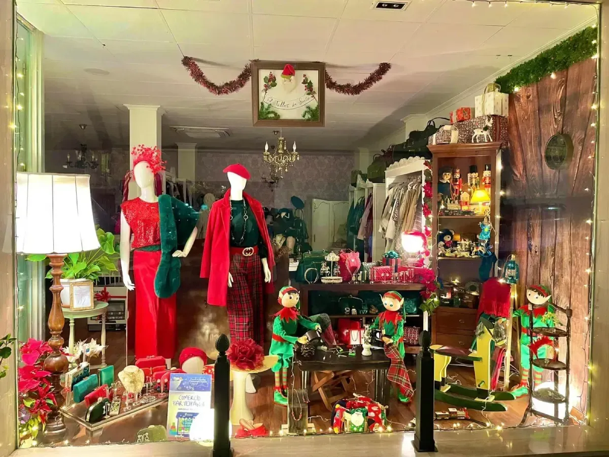 Escaparate con maniquíes vestidos de rojo, adornos navideños y un fondo con forma de árbol.
