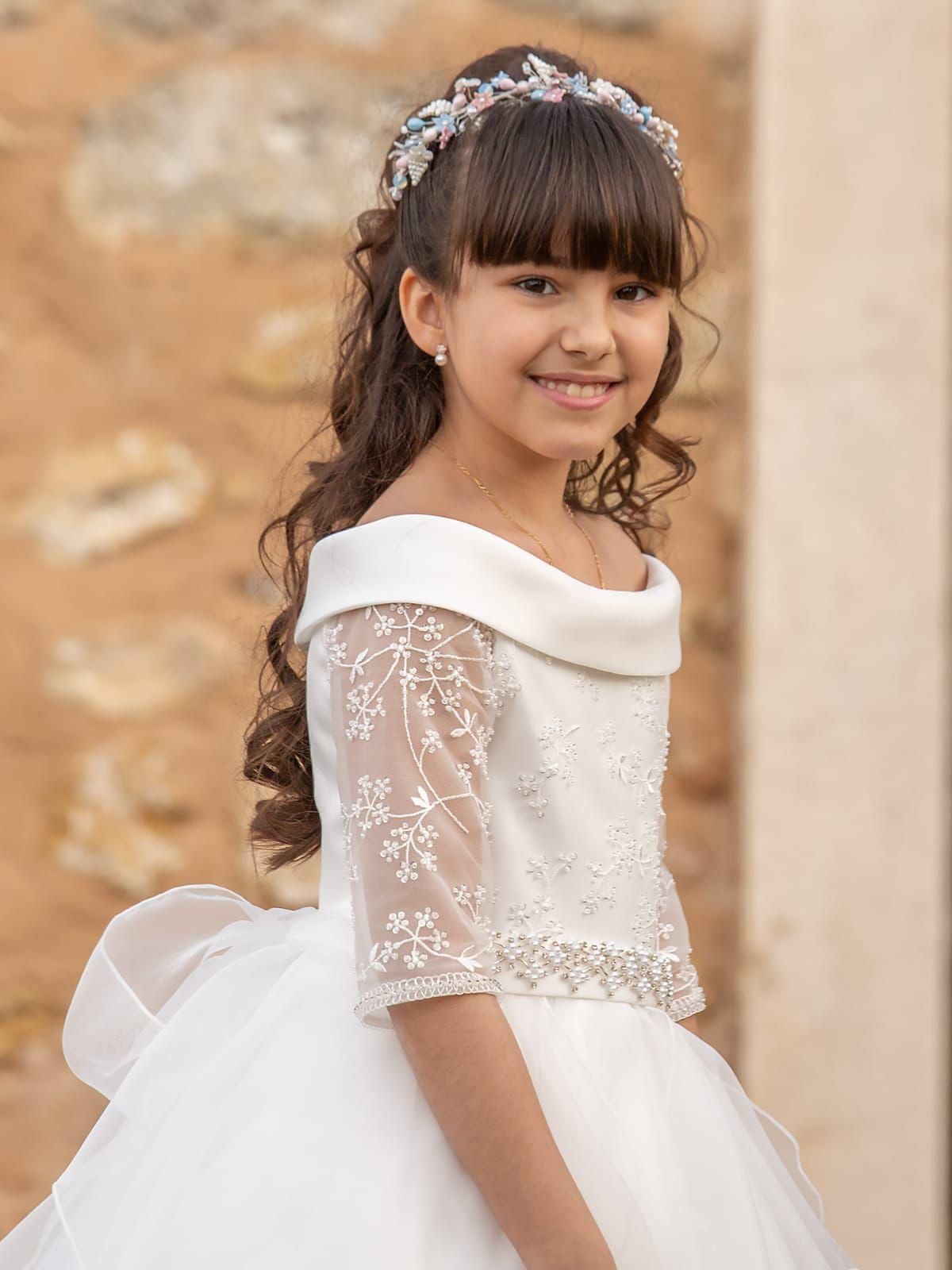 Una chica con un vestido blanco y una diadema con joyas sonríe al aire libre.
