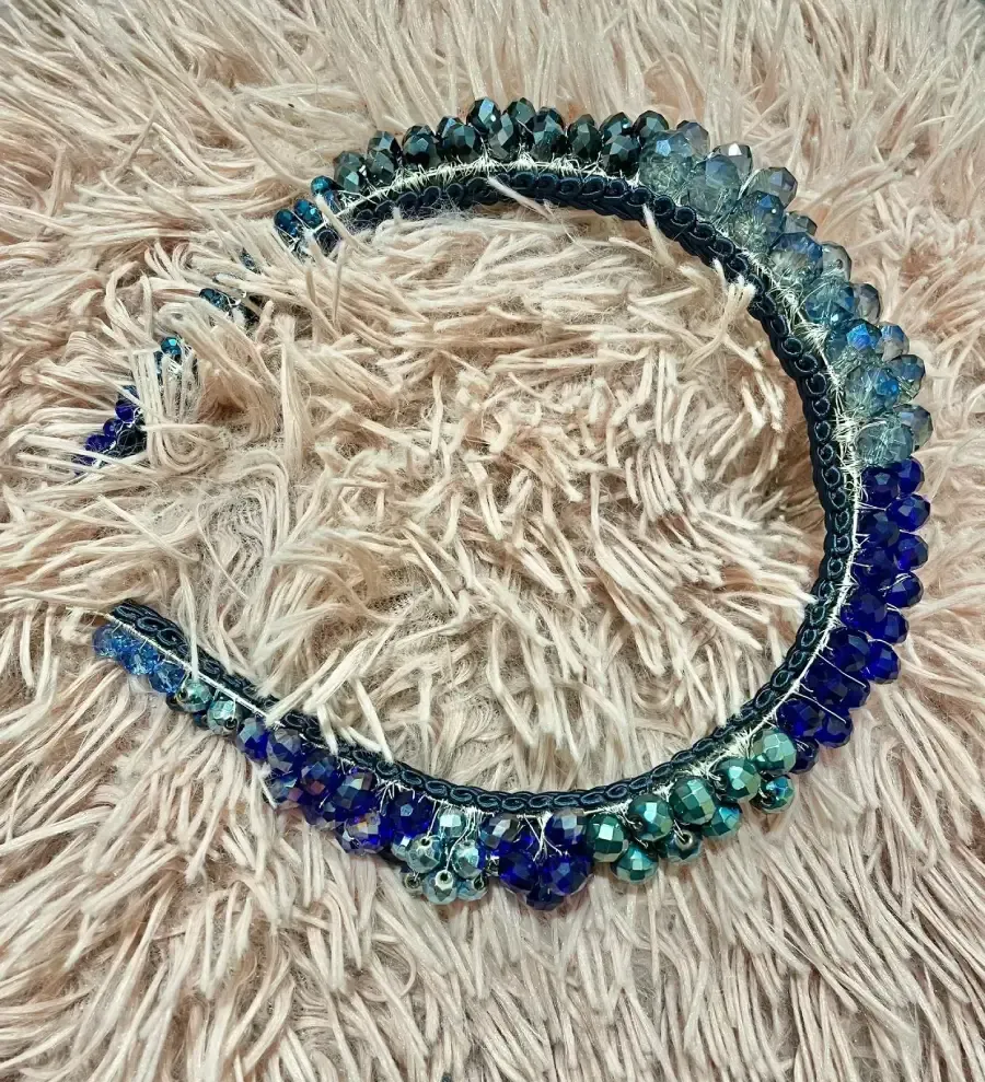Diadema de cuentas azules sobre una superficie esponjosa de color beige. Las cuentas son de varios tonos de azul.