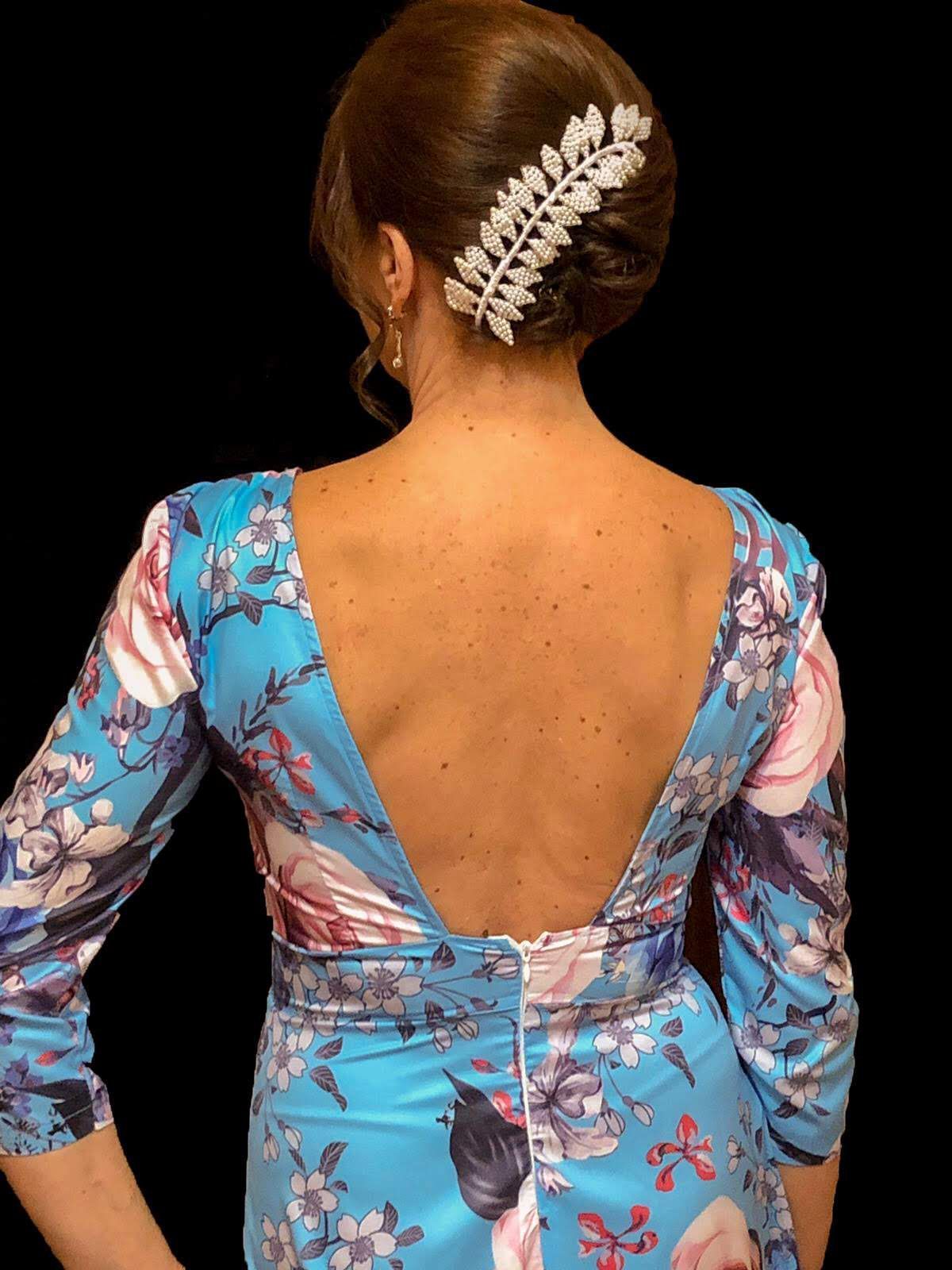 Mujer con vestido floral azul, vista de espaldas, con recogido y horquilla con pedrería. Espalda en V pronunciada.