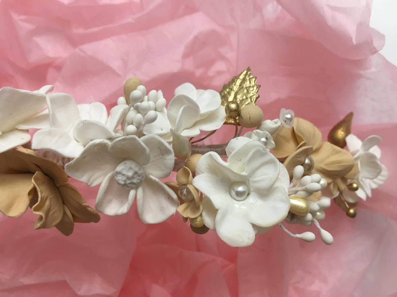Tocado floral con flores blancas, doradas y tostadas, detalles de perlas y una hoja dorada.