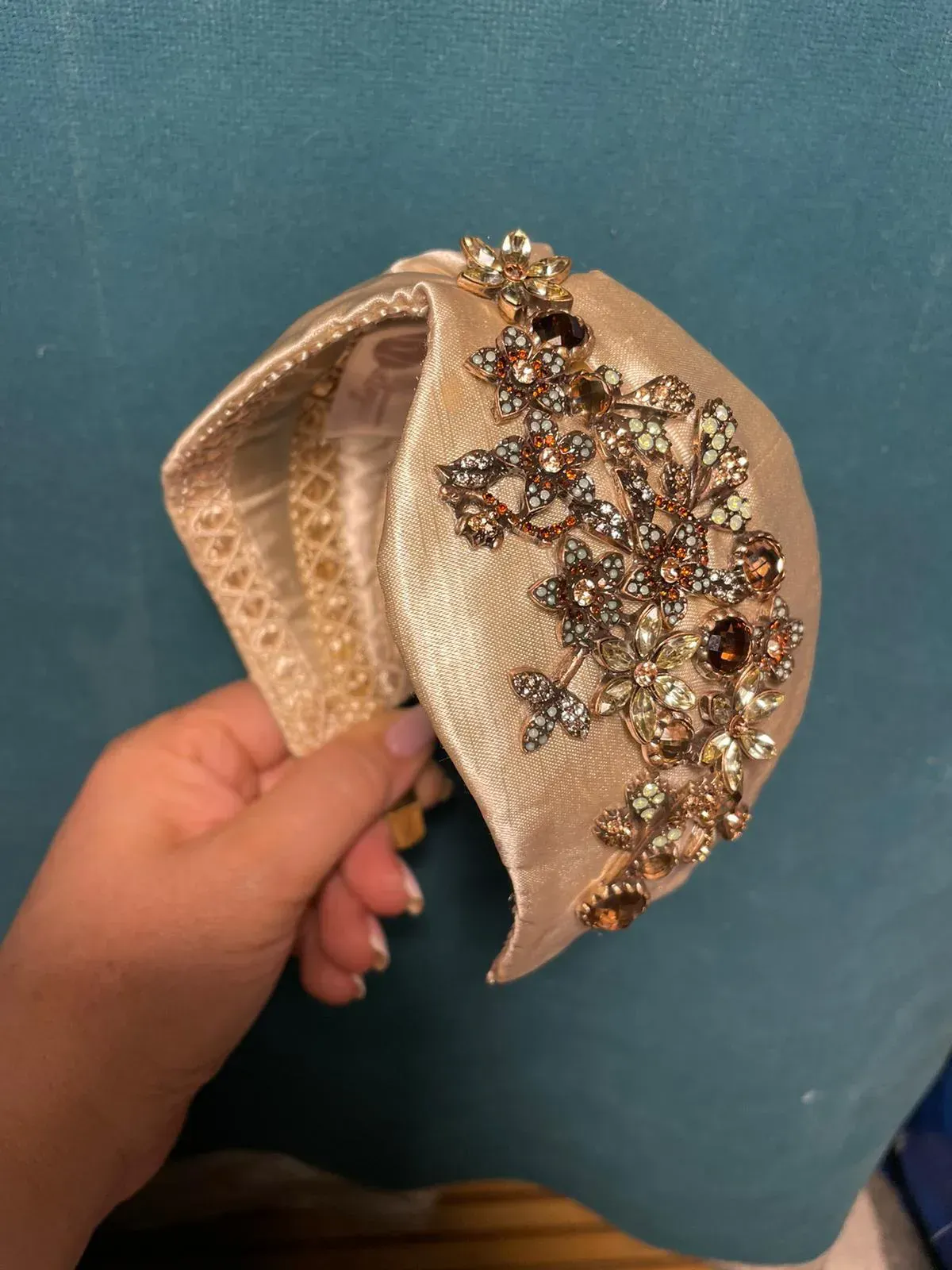 Mano sosteniendo una diadema en tono dorado con un elaborado diseño floral con joyas.