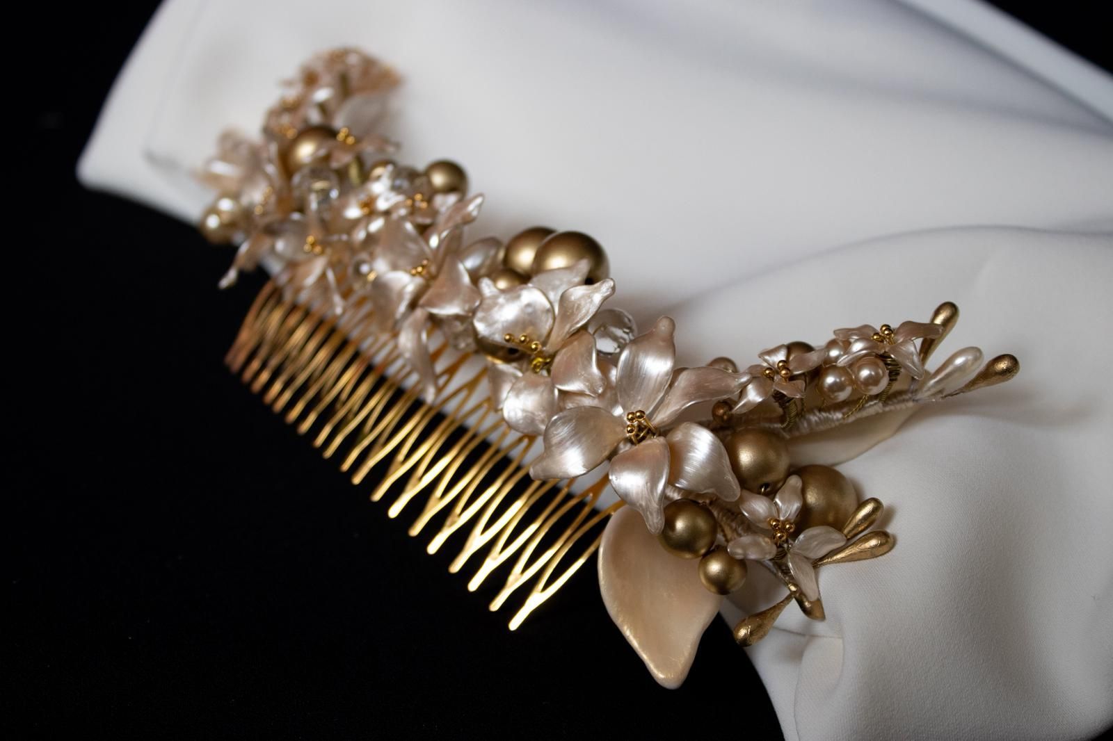 Peineta dorada con detalles de perlas y flores sobre tela blanca.