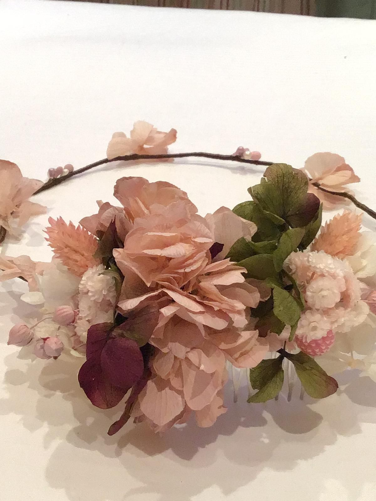 Tocado floral con flores artificiales de color rosa, melocotón y verde y una banda de alambre de color marrón oscuro.