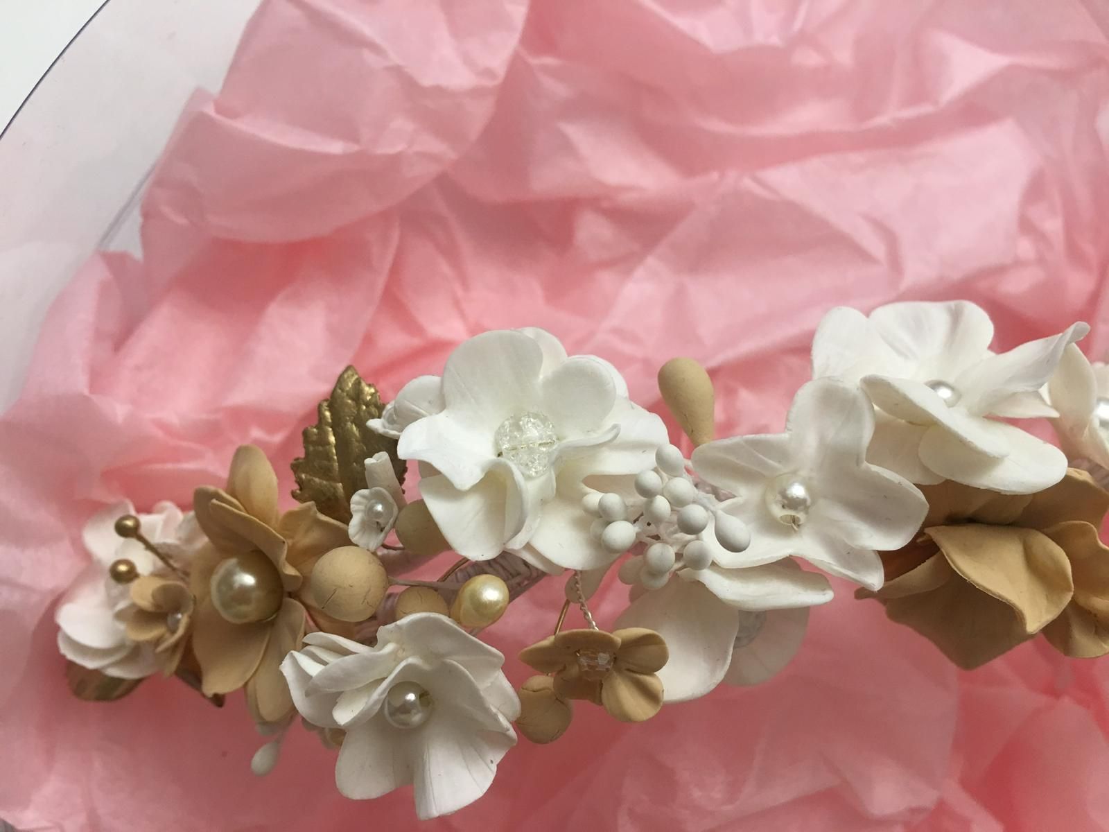 Corona floral para el cabello con flores blancas y doradas y perlas sobre tejido rosa.