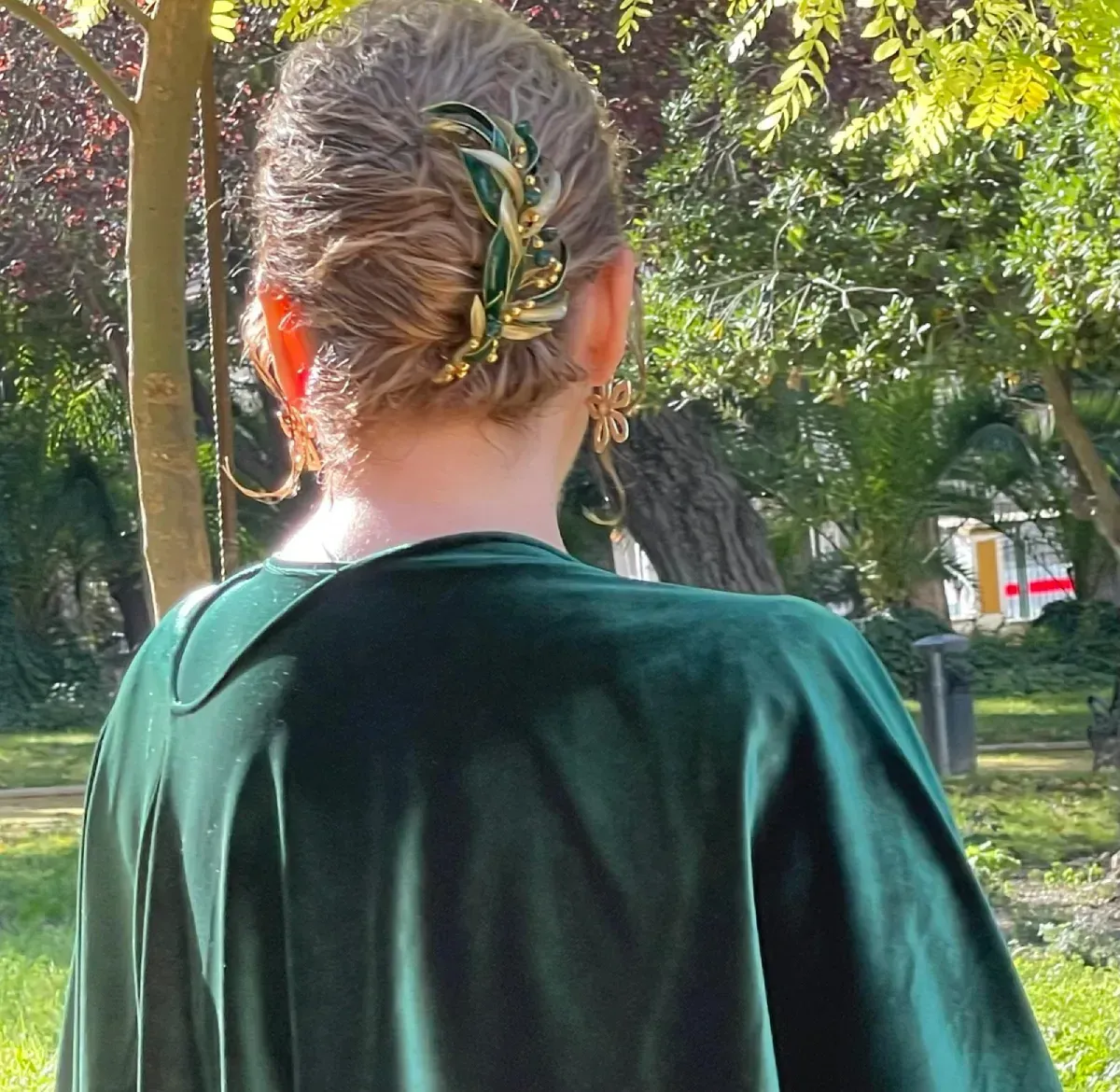 Mujer con vestido de terciopelo verde, cabello recogido con una horquilla decorativa dorada y verde.