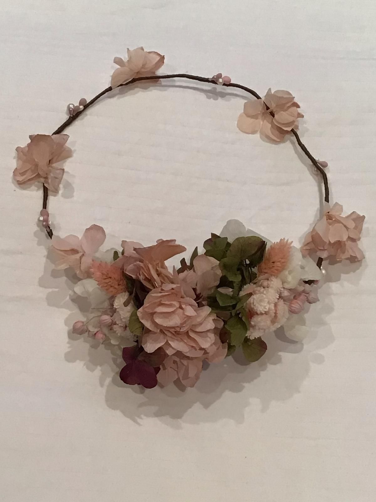 Corona floral con flores rosas y verdes y pequeñas perlas sobre una base de alambre oscuro.