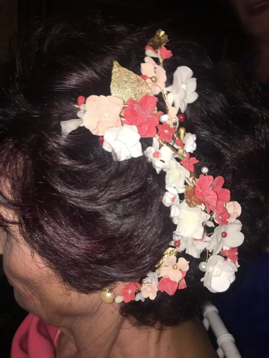 Mujer de cabello oscuro adornada con un tocado floral con flores blancas, rosas y rojas con un acento dorado.