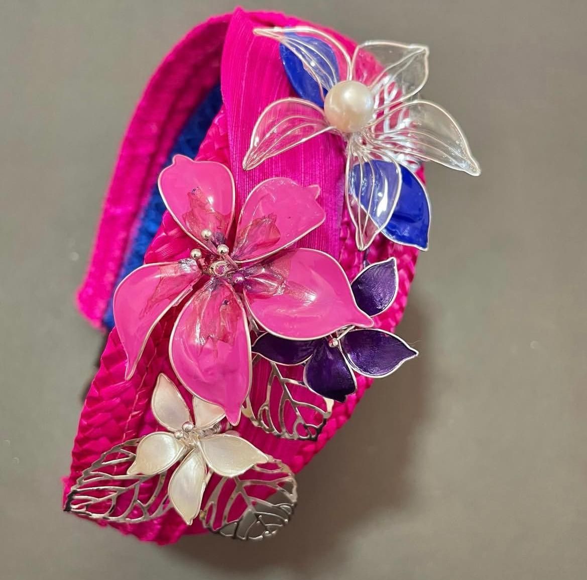 Diadema acanalada de color rosa intenso con adornos florales con bordes plateados en rosa, blanco y azul.