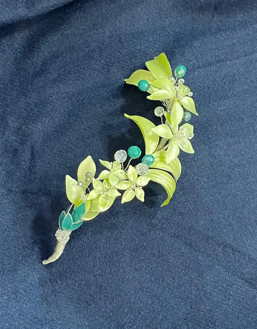 Broche floral verde y plateado con piedras preciosas sobre una superficie azul oscuro.