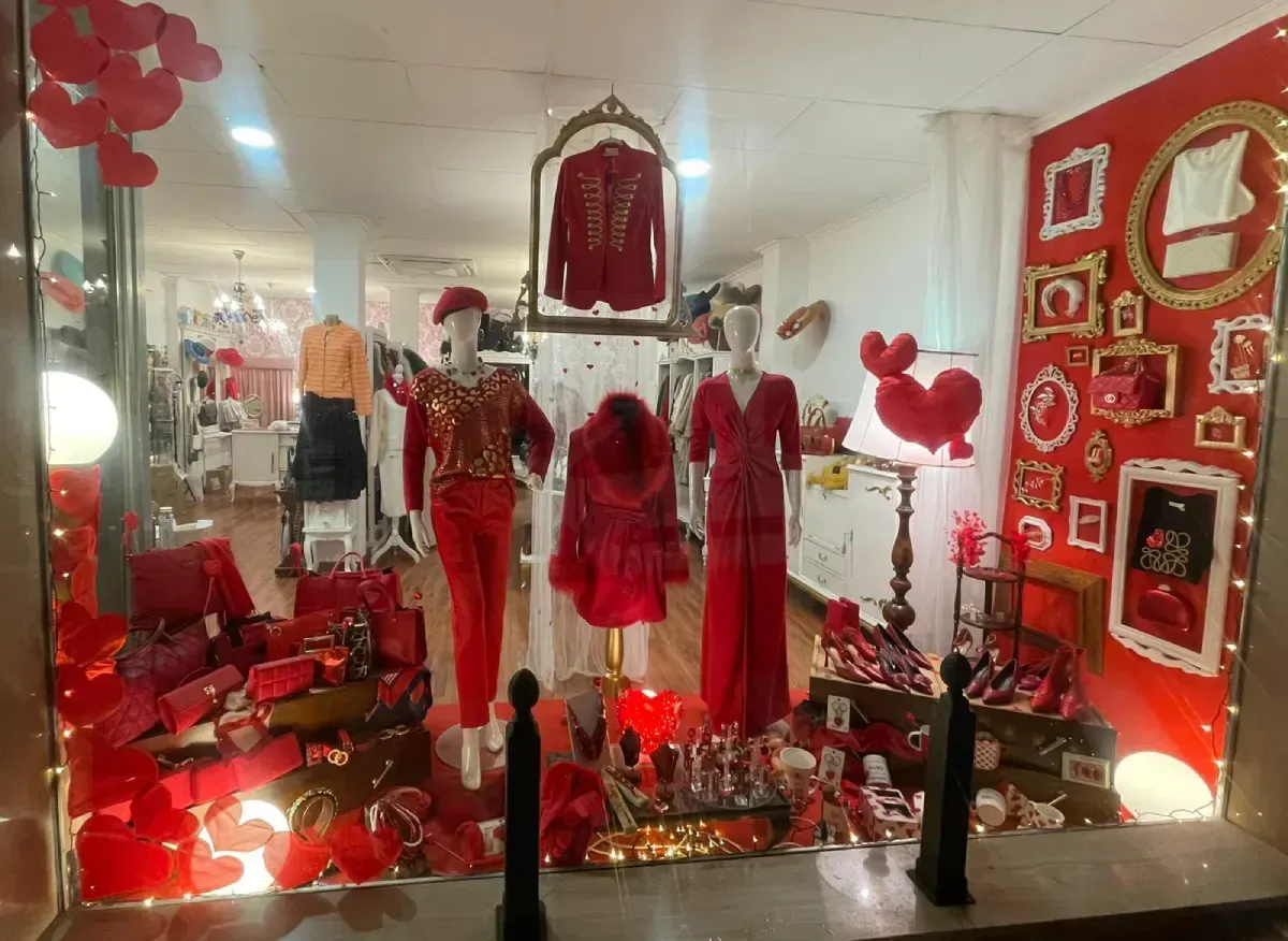 Escaparate con ropa de color rojo y adornos, entre ellos maniquíes y figuras con forma de corazón.