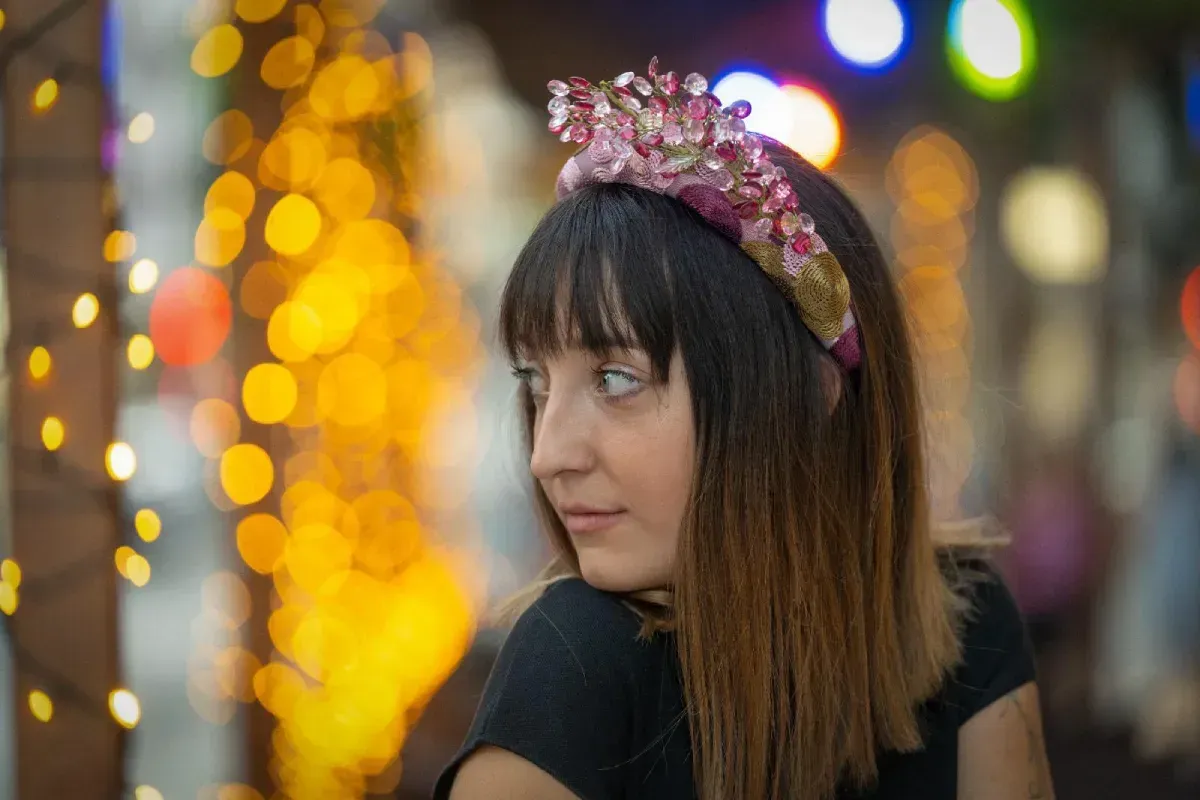 Mujer que lleva una diadema con joyas, mirando por encima del hombro contra un fondo de luces bokeh.