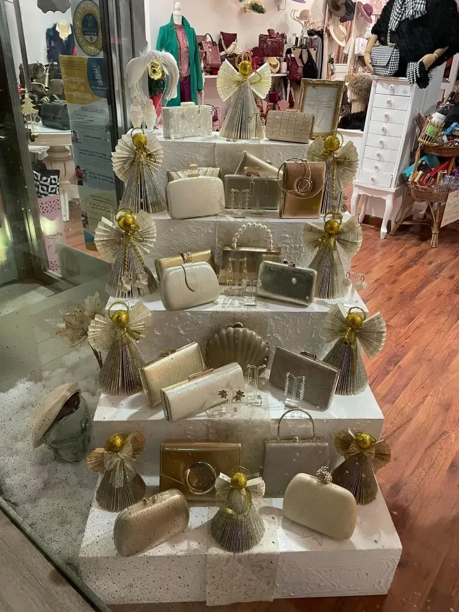 Exhibición de bolsos y accesorios en un escaparate, dispuestos en plataformas escalonadas con decoraciones de ángeles.