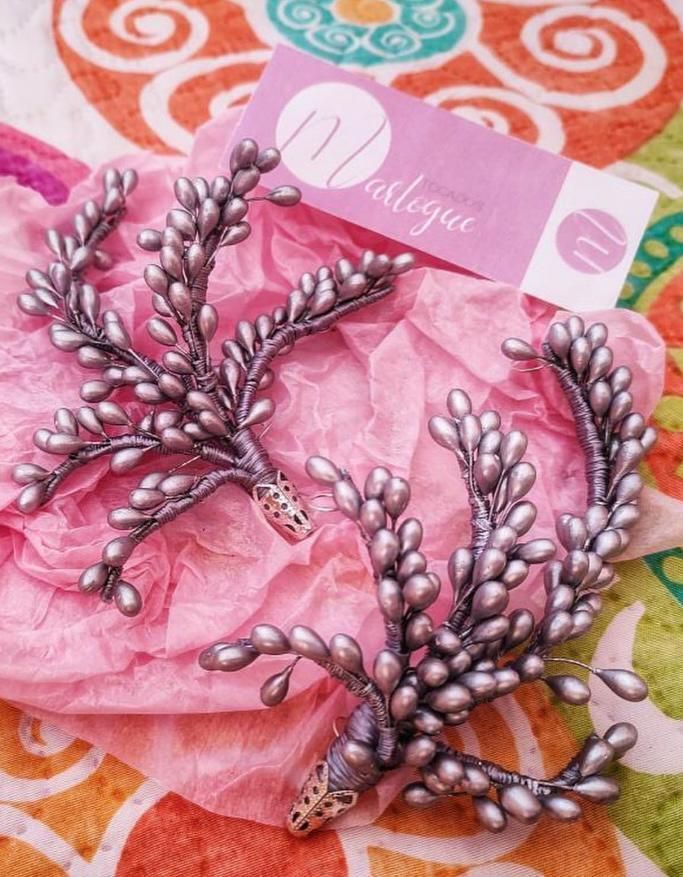 Pinzas para el cabello con cuentas plateadas y diseño floral sobre papel de seda rosa.