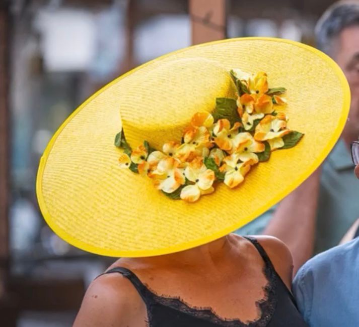 Mujer con un gran sombrero amarillo adornado con flores naranjas y blancas.