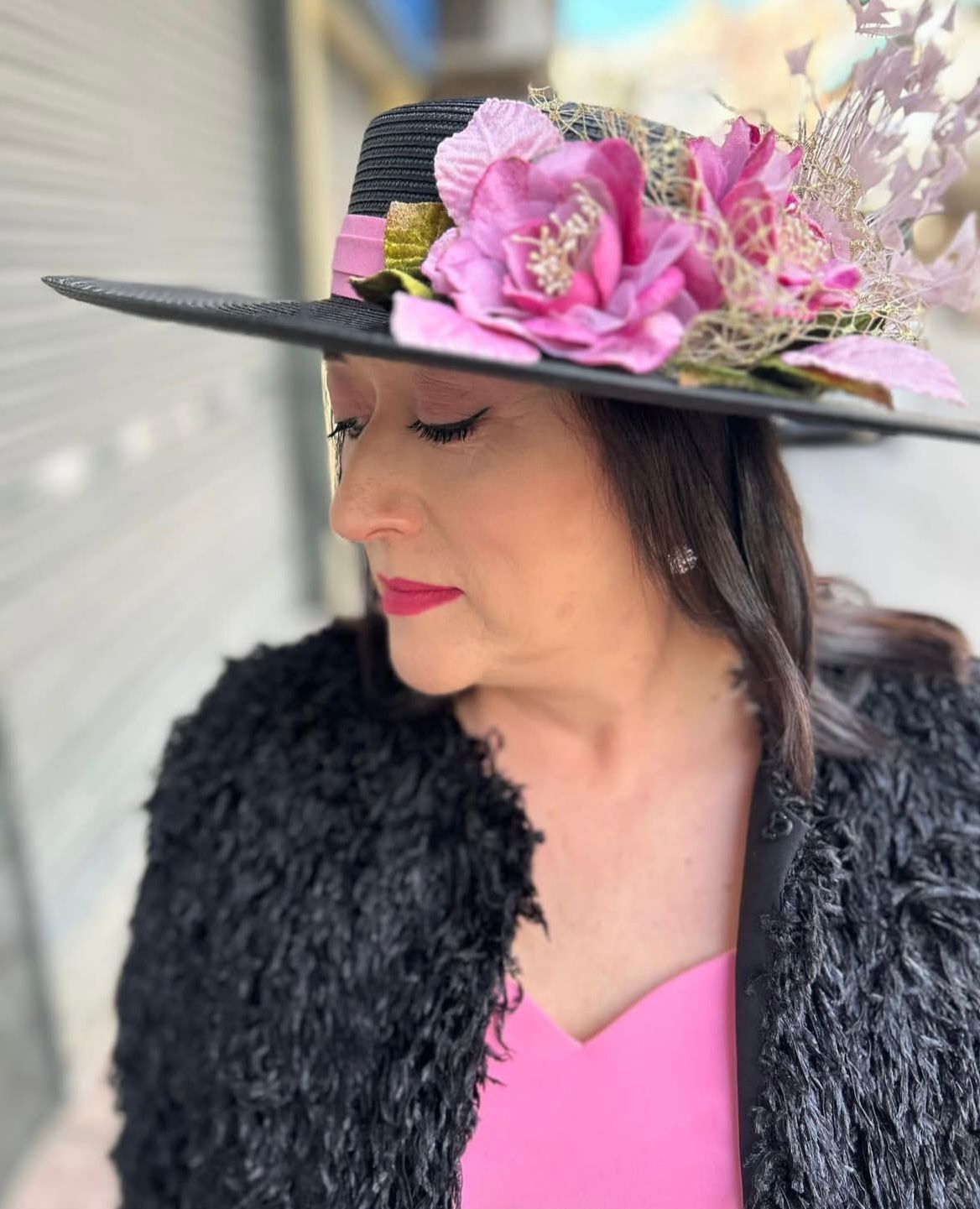 Mujer que lleva un sombrero negro con flores rosas, una chaqueta negra y un top rosa.