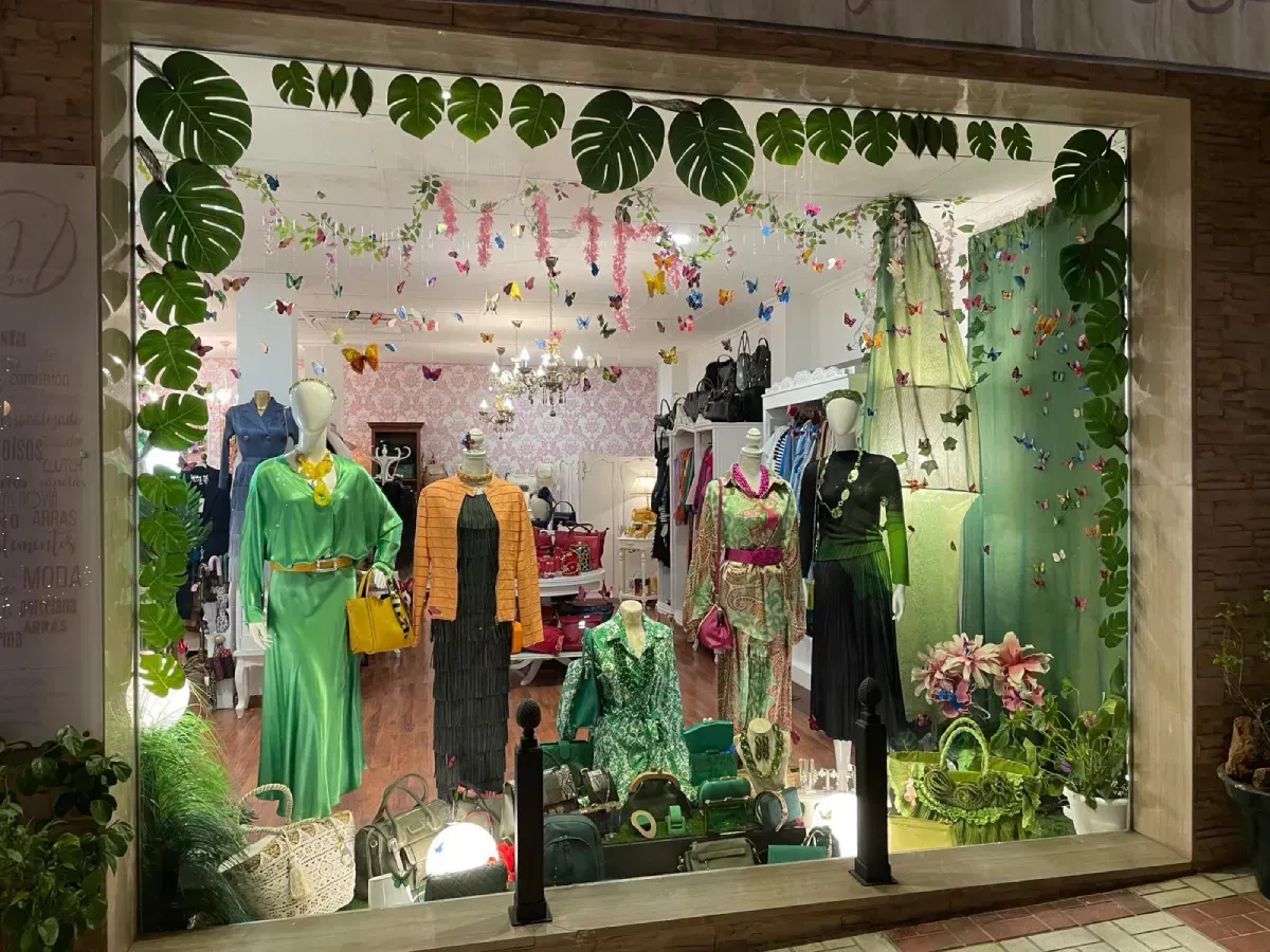 Escaparate de tienda con maniquíes con ropa colorida, adornados con hojas y decoraciones tropicales.
