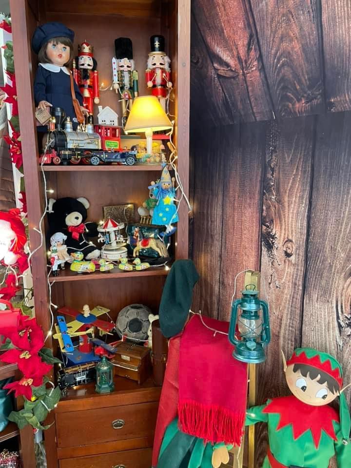 Una estantería navideña con muñecas, cascanueces, juguetes, una lámpara y una figura de elfo.