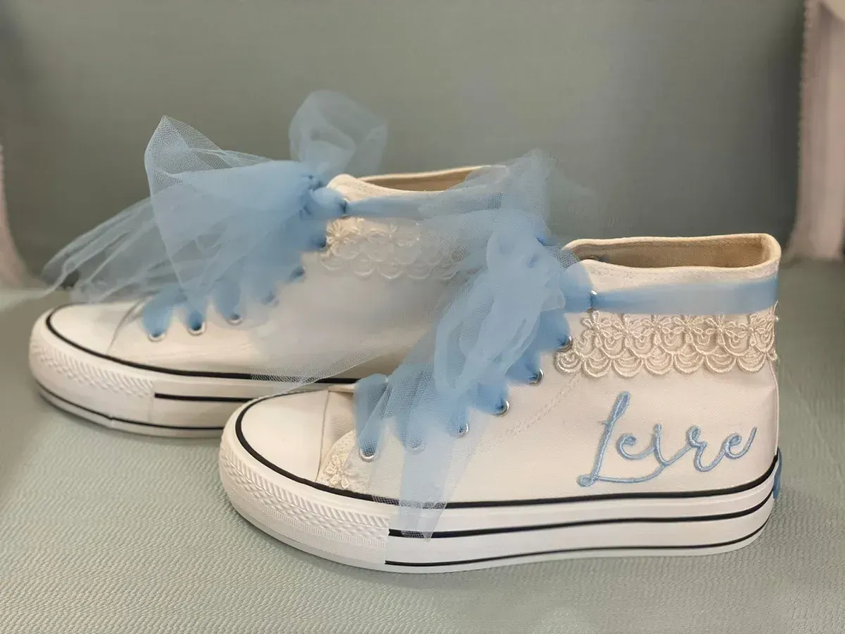 Zapatillas blancas de caña alta con lazos azules y bordado con la palabra