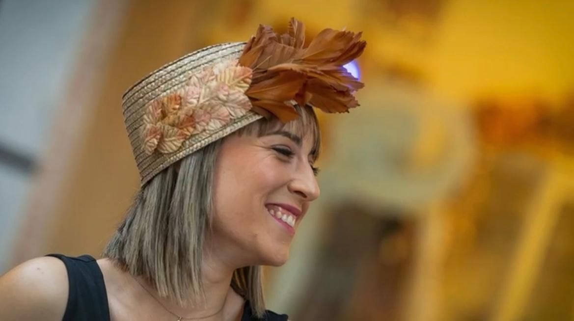 Mujer con sombrero de paja decorado con una gran pluma y sonriendo.