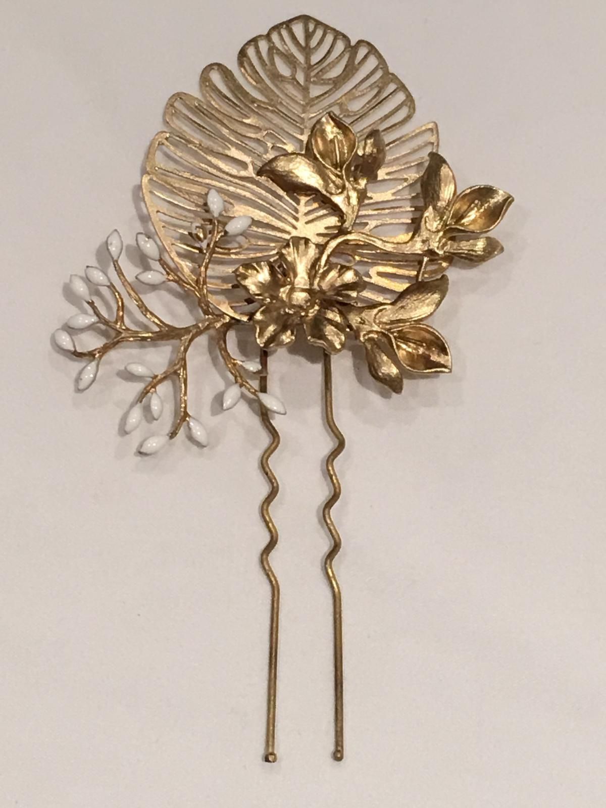 Horquilla dorada con diseño de hojas y flores, detalles en blanco y dos puntas onduladas.