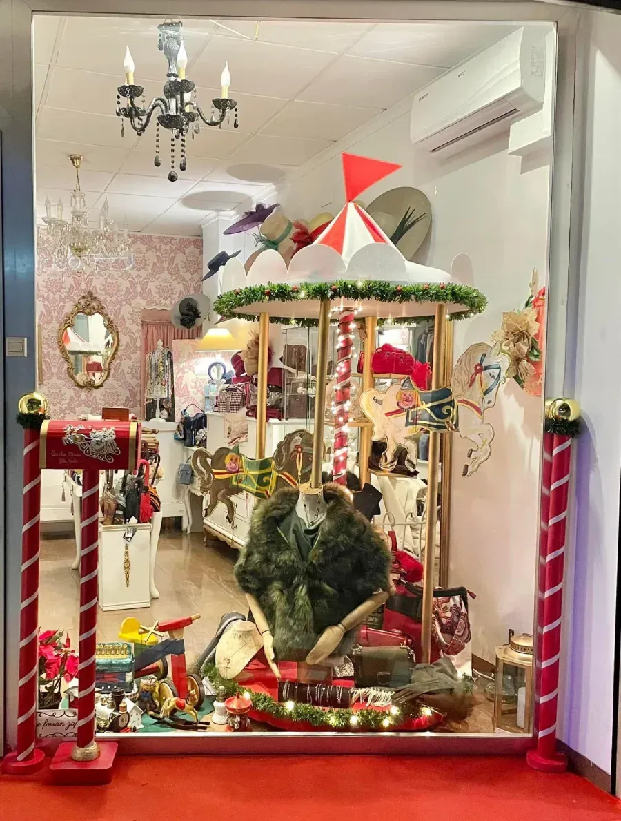 Escaparate de tienda con carrusel de sombreros y adornos festivos.