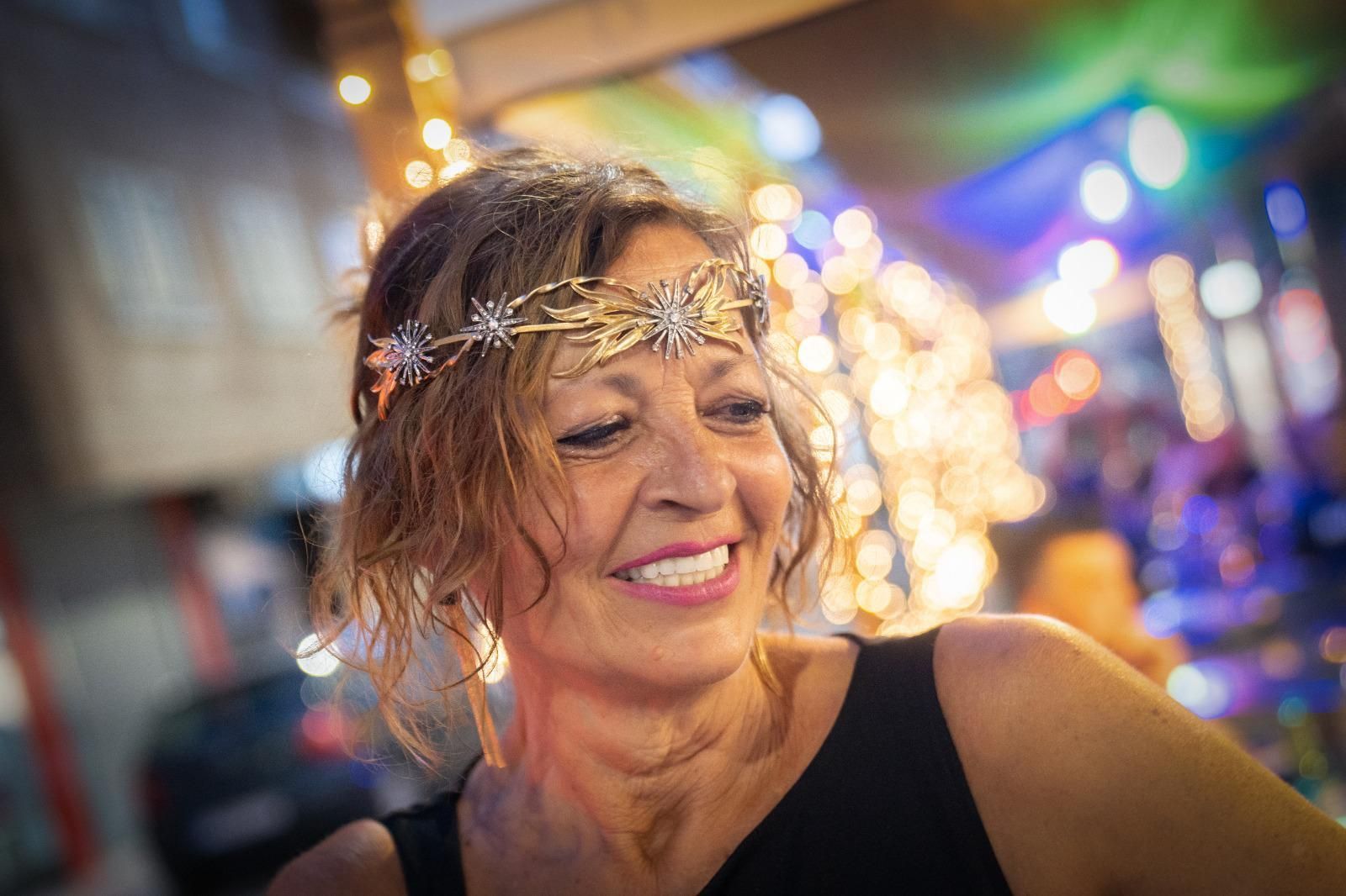 Mujer sonriendo, luciendo una diadema dorada con estrellas, en un evento al aire libre muy iluminado.