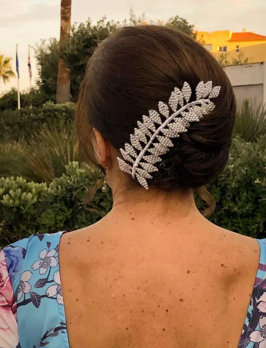 Mujer con cabello castaño recogido y una horquilla con hojas enjoyadas. Vista trasera, al aire libre.