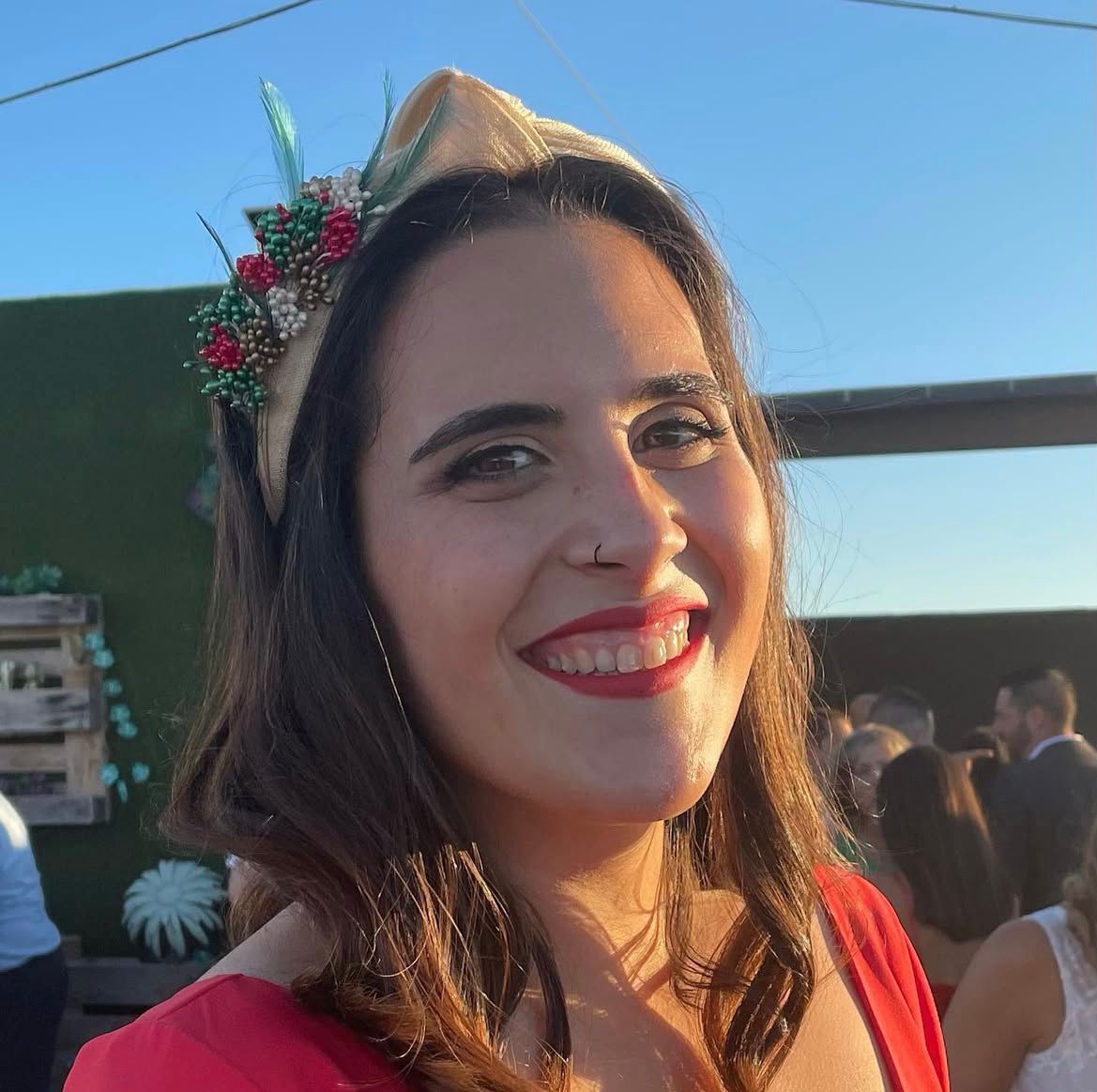 Una mujer con un vestido rojo y una diadema decorada sonríe al aire libre.