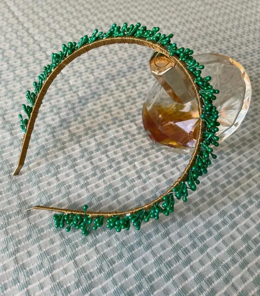 Diadema dorada con adornos de cuentas verdes, sobre una superficie estampada.