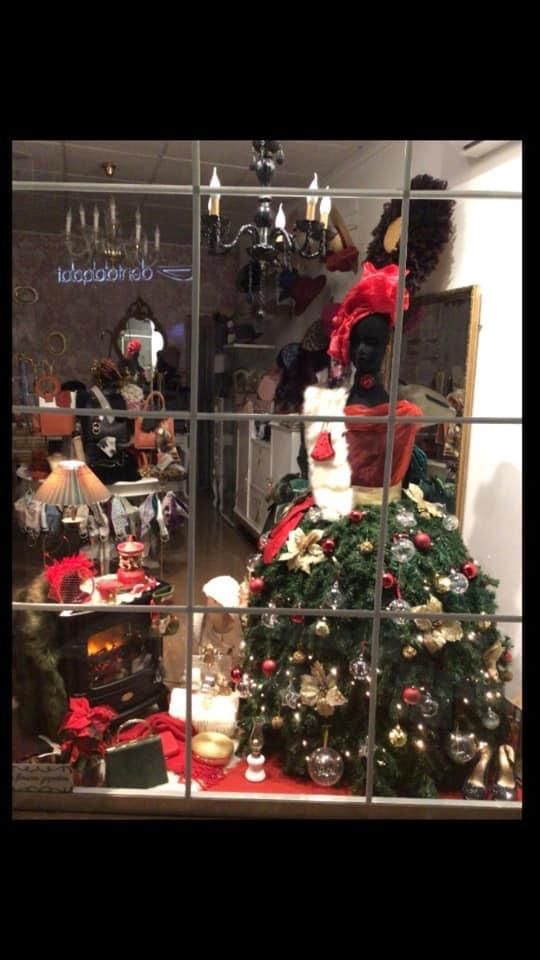 Escaparate navideño con árbol, adornos, acentos rojos y reflejos.