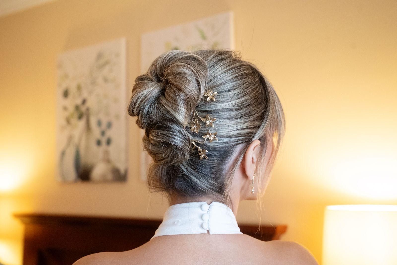 Mujer con peinado recogido gris decorado con alfileres dorados, de pie en el interior, con un vestido blanco.