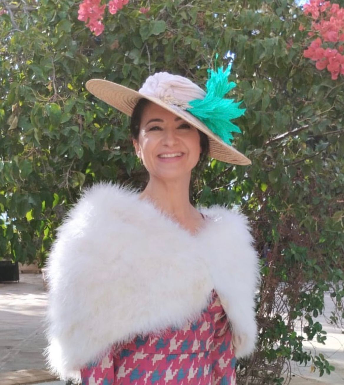 Mujer con un sombrero de paja con detalles de plumas y un chal blanco, sonriendo al aire libre.